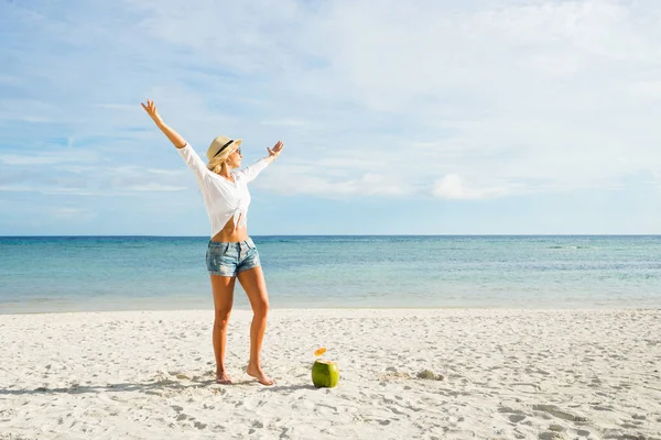 ココナッツが付いている浜に上げられた手を幸せな女は 青い海と空を背景に — ストック写真