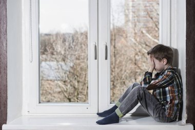 Genç çocuk tek başına oturmak penceresinde ağlıyor ve ellerini yüzüne gizle.
