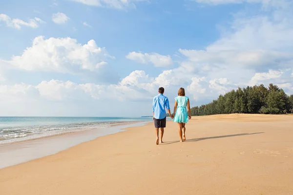Young beautiful couple walking away on sandy beach. Back view.