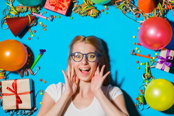 Happy birthday and holidays concept. Young woman in glasses, gift boxes and holidays accessories on blue background. Overhead view. Focus on woman face.