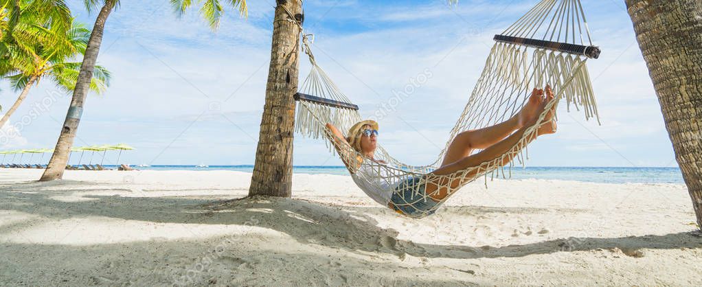 Woman in hat relaxing on hammock on the beach. Travel and vacation concept. Banner edition.