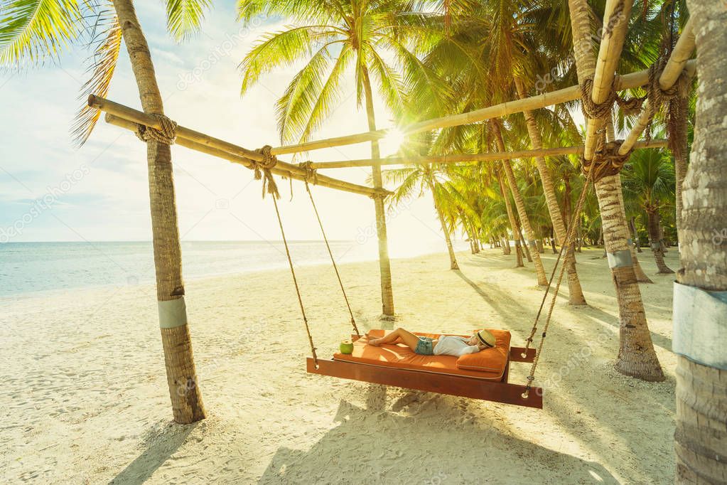 Woman with coconut relaxing on the beach between palms. Vacation concept.