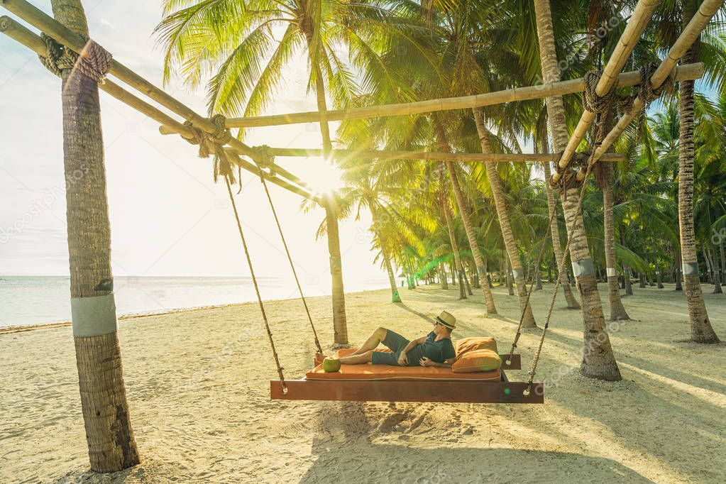 Man with coconut relaxing on the beach between palms. Vacation concept.