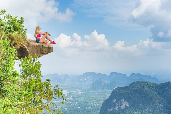 愉快的年轻女孩坐在山顶与山谷和岩石的风景的令人惊叹的看法 — 图库照片