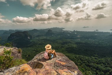 Sırt çantalı genç bir kadın dağın tepesinden manzaranın nefes kesici manzarasının tadını çıkarıyor. Seyahat kavramı. Arka plan.
