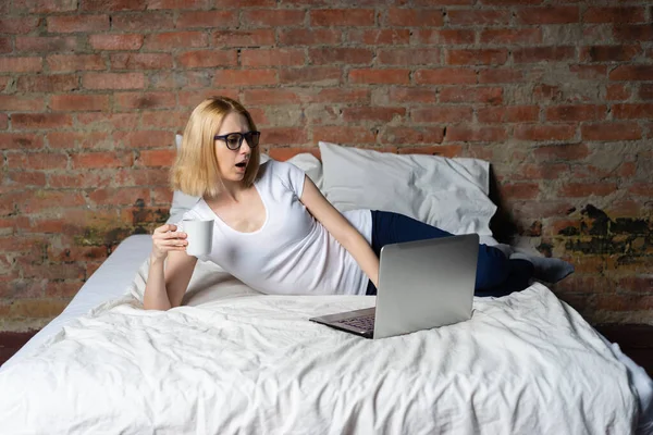 Shocked young woman in bed looking something in laptop.