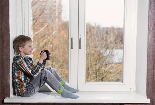 Child sitting on window with cup of tea.