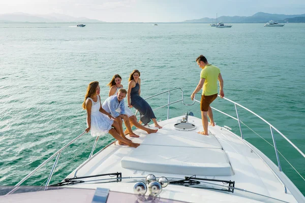 Young people sitting on the yacht deck, sailing the sea. Friendship and luxury vacation concept.