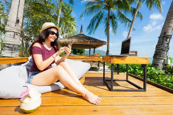 坐在海滨咖啡馆里 拿着笔记本电脑和椰子 用智能手机的女人 — 图库照片