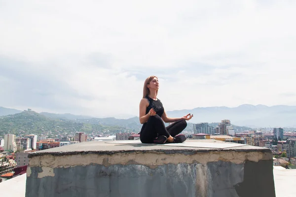 屋根の上のマットでヨガを練習する女性 ヨガの練習や瞑想をしている女の子 町や山を背景に — ストック写真