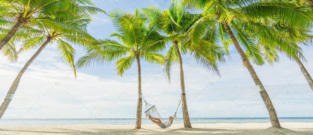 Woman lying on hammock between palms on the beautiful tropical beach. Travel and vacation concept. Banner and panoramic edition.
