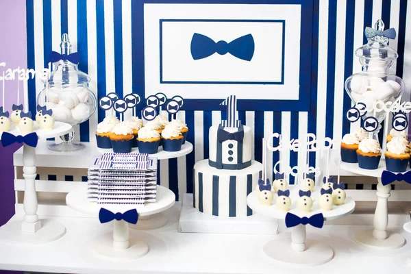 Pasteles, caramelos, malvaviscos, pastelitos, chocolate y otros dulces en la mesa de postres en la fiesta de cumpleaños de los niños. Barra de dulces de celebración de postre de cumpleaños en colores blanco y azul . — Foto de Stock