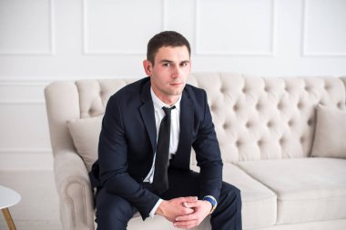 Kanepede oturan ve kameraya bakarak bir takım genç bir ciddi ve kendine güvenen adam portresi.