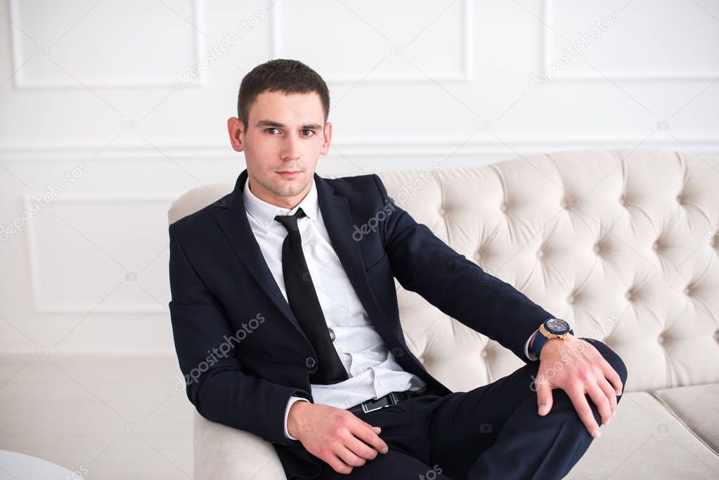 Portrait of a young serious and confident man in a suit sitting on the couch and looking at camera.