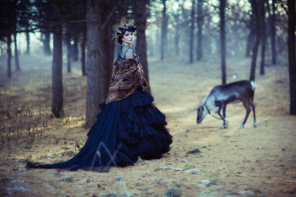 Girl in a lush black skirt and deer in the autumn forest