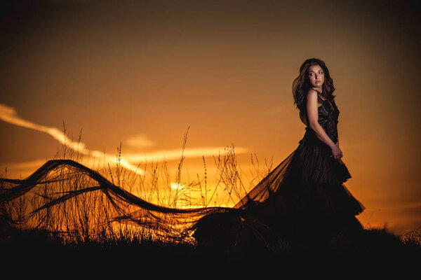 A girl in a long dress against the background of an orange sunset