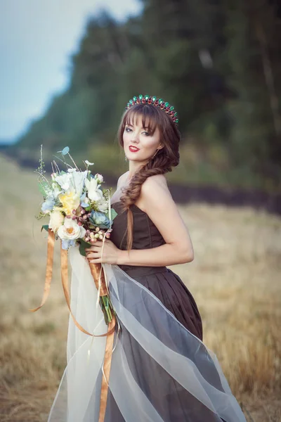 Mulher em um campo com um buquê de flores — Fotografia de Stock