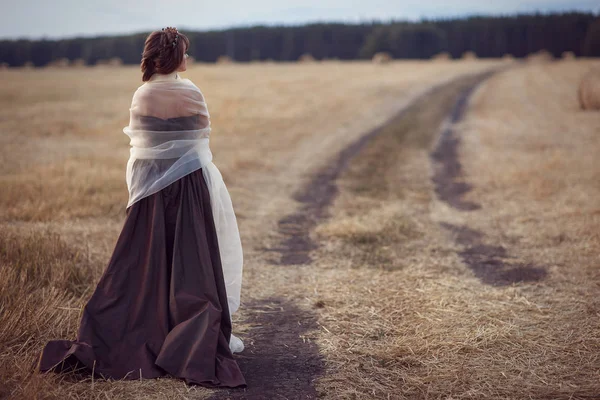 Het meisje staat in het veld door de weg — Stockfoto