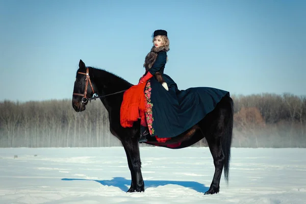 Een meisje in een lange zwarte jurk met een donker paard — Stockfoto