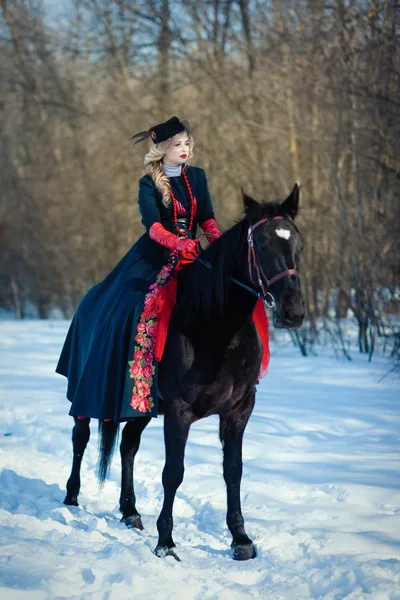 Uma menina em um vestido preto longo com um cavalo escuro — Fotografia de Stock