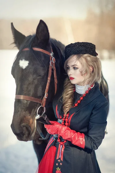 Uma menina em um vestido preto longo com um cavalo escuro — Fotografia de Stock