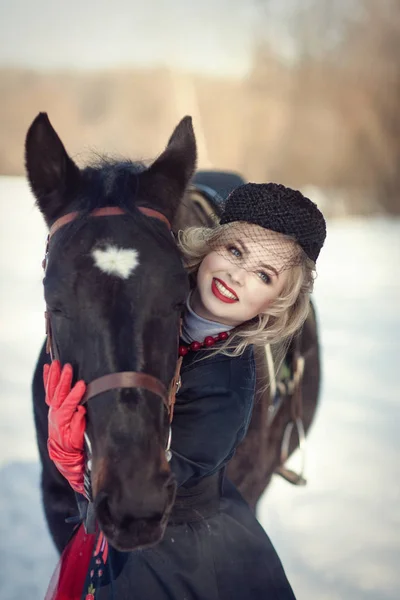 Uma menina em um vestido preto longo com um cavalo escuro — Fotografia de Stock
