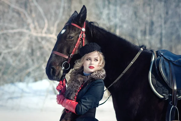 Uma menina em um vestido preto longo com um cavalo escuro — Fotografia de Stock