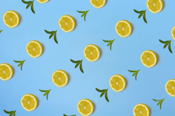 Trendy sunlight Summer pattern made with yellow lemon slice and fresh mint leaves on bright light blue background. Minimal summer concept.