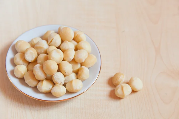 Köstliche Macadamia-Nüsse auf Teller auf Holzgrund — Stockfoto