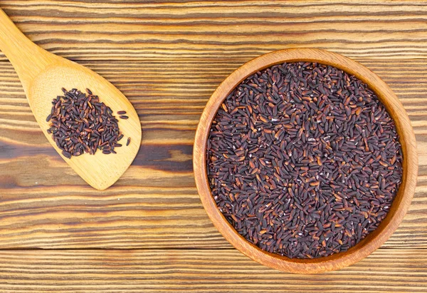 Ahşap arka plan üzerinde kapta çiğ siyah pirinç 