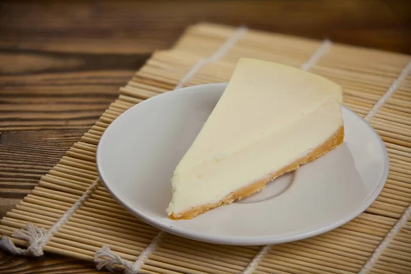 木製テーブルの上の白い皿に古典的なチーズケーキ — ストック写真