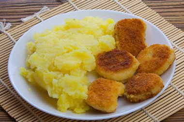 Tabakta haşlanmış patates püresi ve masada tavuk nugget.