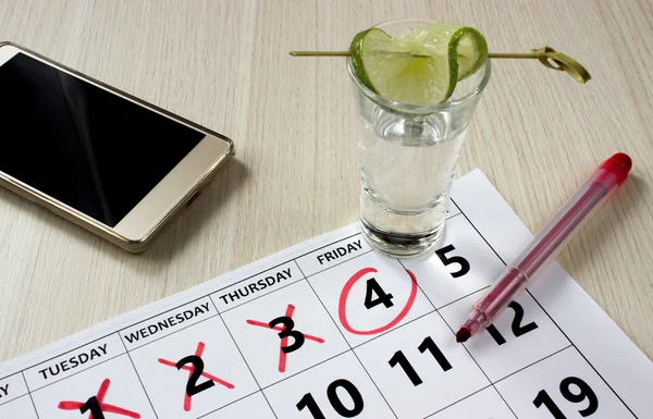 Red color writing on the calendar at friday with shot of tequila with a slice of lime and phone