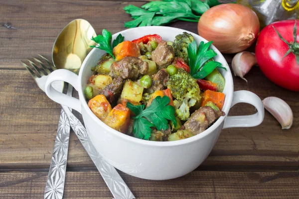 Served beef meat stewed with vegetables in ceramic pot with ingredients on wooden background — Stock Photo, Image