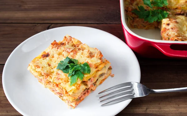 Close-up of a traditional lasagna topped with parskey leafs served on a white plate with fork — Stock Photo, Image