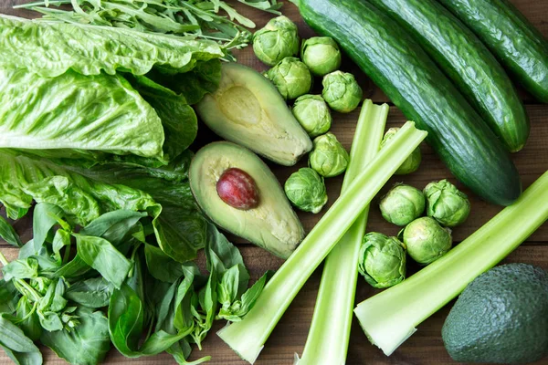 Productos que contienen ácido fólico - vitamina B9. Verduras verdes sobre fondo de madera. Apio, rúcula, aguacate, coles de Bruselas, albahaca, pepino, ensalada romana —  Fotos de Stock