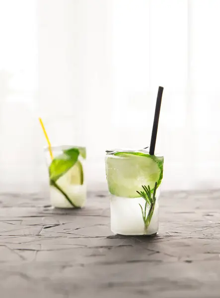 Two glasses with fresh cocktail made of ice on concrete table in front of window — Stock Photo, Image