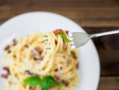 tabak makarna Carbonara ve spagetti eski ahşap masa üzerinde bir çatalı üzerinde pastırma ve parmesan peyniri ile