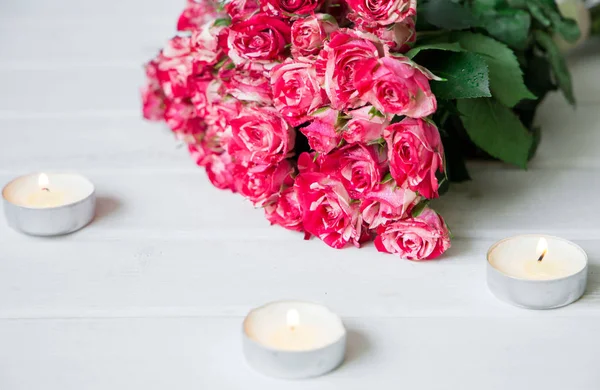 Beautiful pink roses with candles on a white wooden surface — Stock Photo, Image