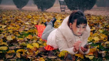Güzel kadın çekici makyaj ile sonbahar Park düşen yapraklar yatan telefonda konuşmaya başladı.
