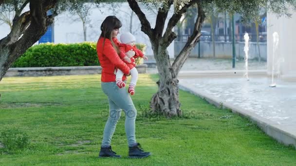 Jovem mãe com bebê em seus braços caminhando para a fonte — Vídeo de Stock