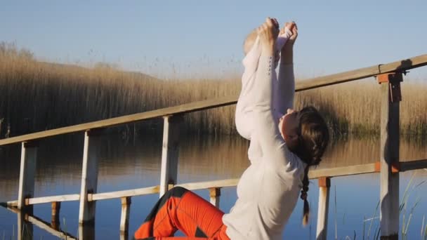 Мати виховує дитину руками на березі ставка на заході сонця . — стокове відео