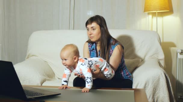 Mother and blue eyed baby sitting on white couch watching video on laptop screen — Stock Video