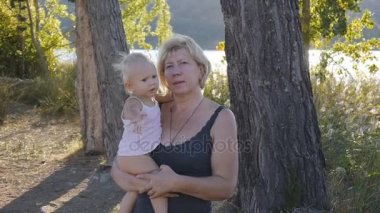 Sarışın bebek kız doğal arka plan üzerinde günbatımında poz elinde olan orta yaşlı beyaz kadın