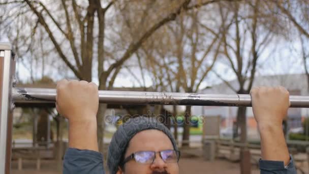 Entrenamiento callejero para principiantes. Primer plano de regordete hispano hombre en gafas tratando de hacer barbilla-ups en el gimnasio al aire libre bar . — Vídeo de stock