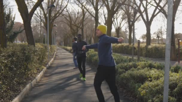 Entrenamiento callejero de equipo multirracial. Grupo deportivo de jóvenes multiétnicos haciendo warmup running y twisting en el parque como parte de una rutina de entrenamiento . — Vídeos de Stock