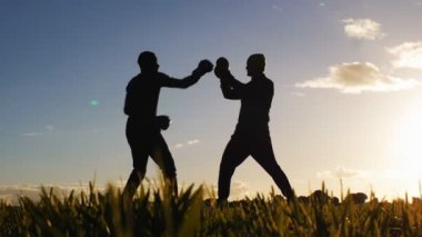Boks egzersiz ile eğitmen açık havada. Düşük açılı rakipler siluetleri boks eldiven bir alanda gün batımında fikir tartışması bir kadeh. Üçlü yumruk vurmayı öğrenme avcı.