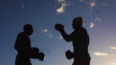 Boks egzersiz ile eğitmen açık havada. Boksörler boks eldivenleri siluetleri mavi bulutlu fikir tartışması arka plan gökyüzü. Bir yumruk birden kenara çekilip kurtulmak için pratik.