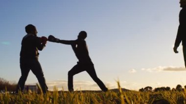 Boks egzersiz ile eğitmen açık havada. Düşük açılı rakipler siluetleri boks eldiven bir alanda gün batımında fikir tartışması bir kadeh. Avcı vurmayı öğrenme.