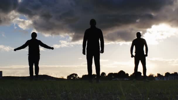 Allenamento su strada di una squadra multirazziale. Silhouette di giovani uomini multietnici che fanno riscaldamento saltando sul posto su sfondo cielo nuvoloso come parte di una routine di allenamento . — Video Stock